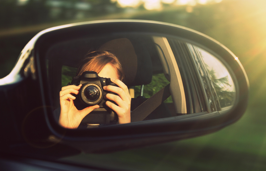 Frau fotografiert sich in einem Auto-Seitenspiegel