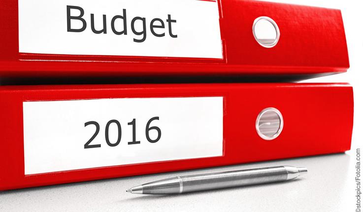 zwei rote, waagerecht aufeinander liegende Ordner mit den Aufschriften "Budget" und "2016" mit davor liegendem silbernen Kugelschreiber vor weißem Hintergrund 