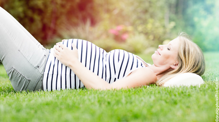 blonde schwangere Frau mit weiß-blau gestreiftem Top lächelt auf dem Boden liegend mit Blick zu ihrem Bauch