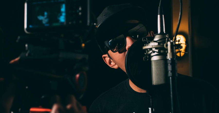 Mann mit Sonnenbrille steht hinter einem Mikro im Studio