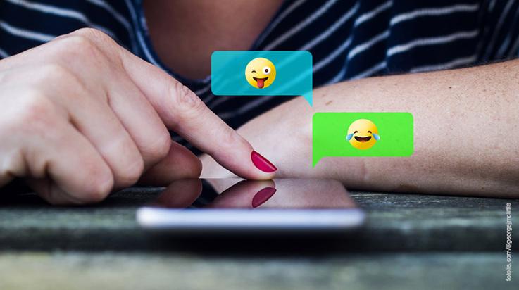 Person tippt Emojis auf Handydisply ein
