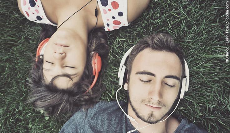 Mann und Frau liegen im Gras und tragen Kopfhörer