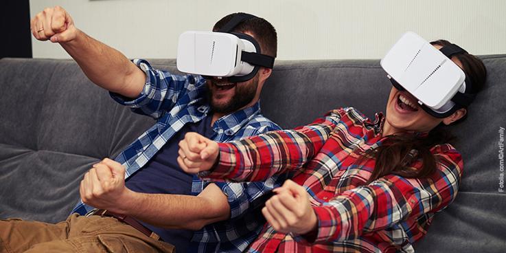 Mann und Frau mit Virtual Reality Brille sitzen lenkend auf einem Sofa