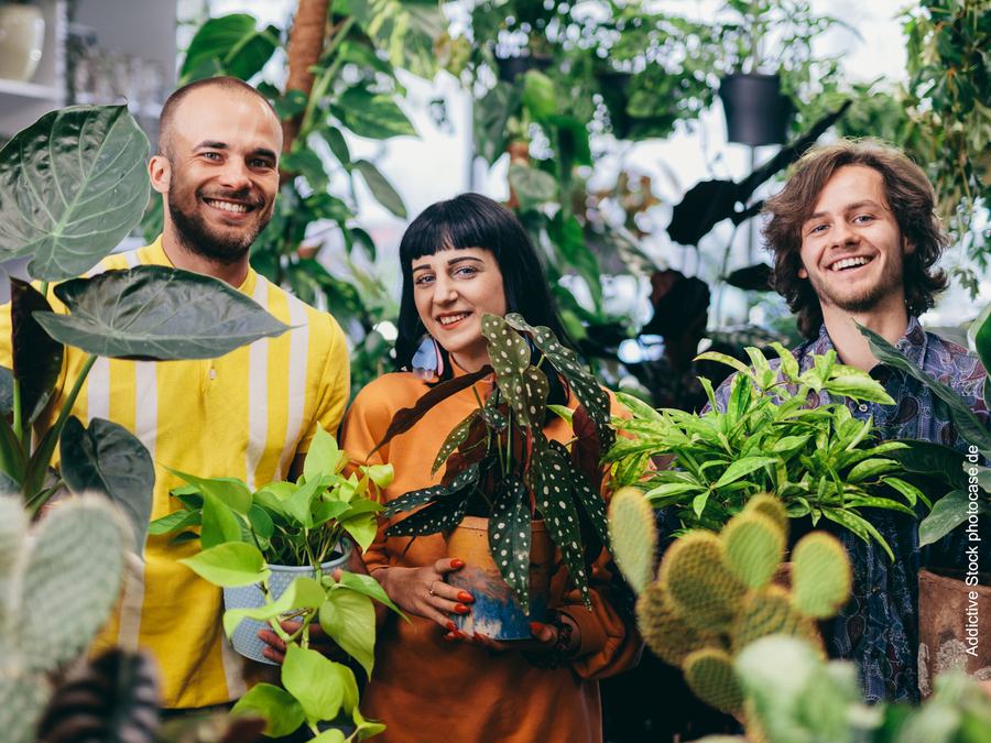 Drei junge Menschen blicken in umringt vomn Pflanzen in die Kamera